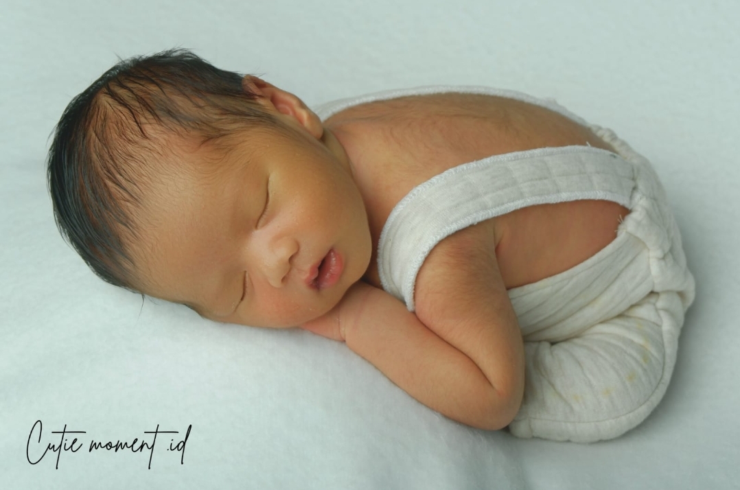 Foto bayi pose tidur di atas kain putih